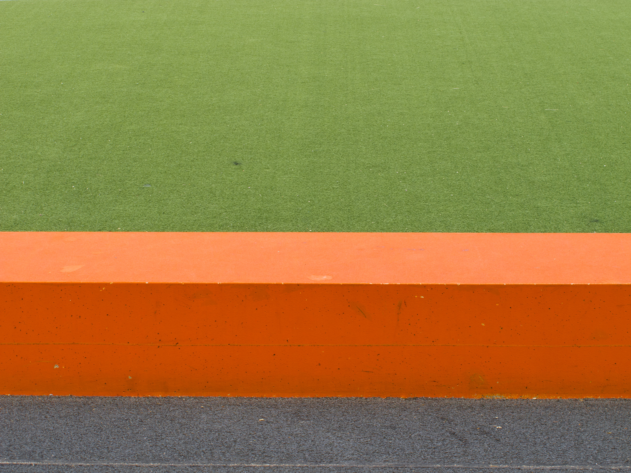 ein grüner Fußballplatzrasen mit einer orangenen kleinen Mauer davor