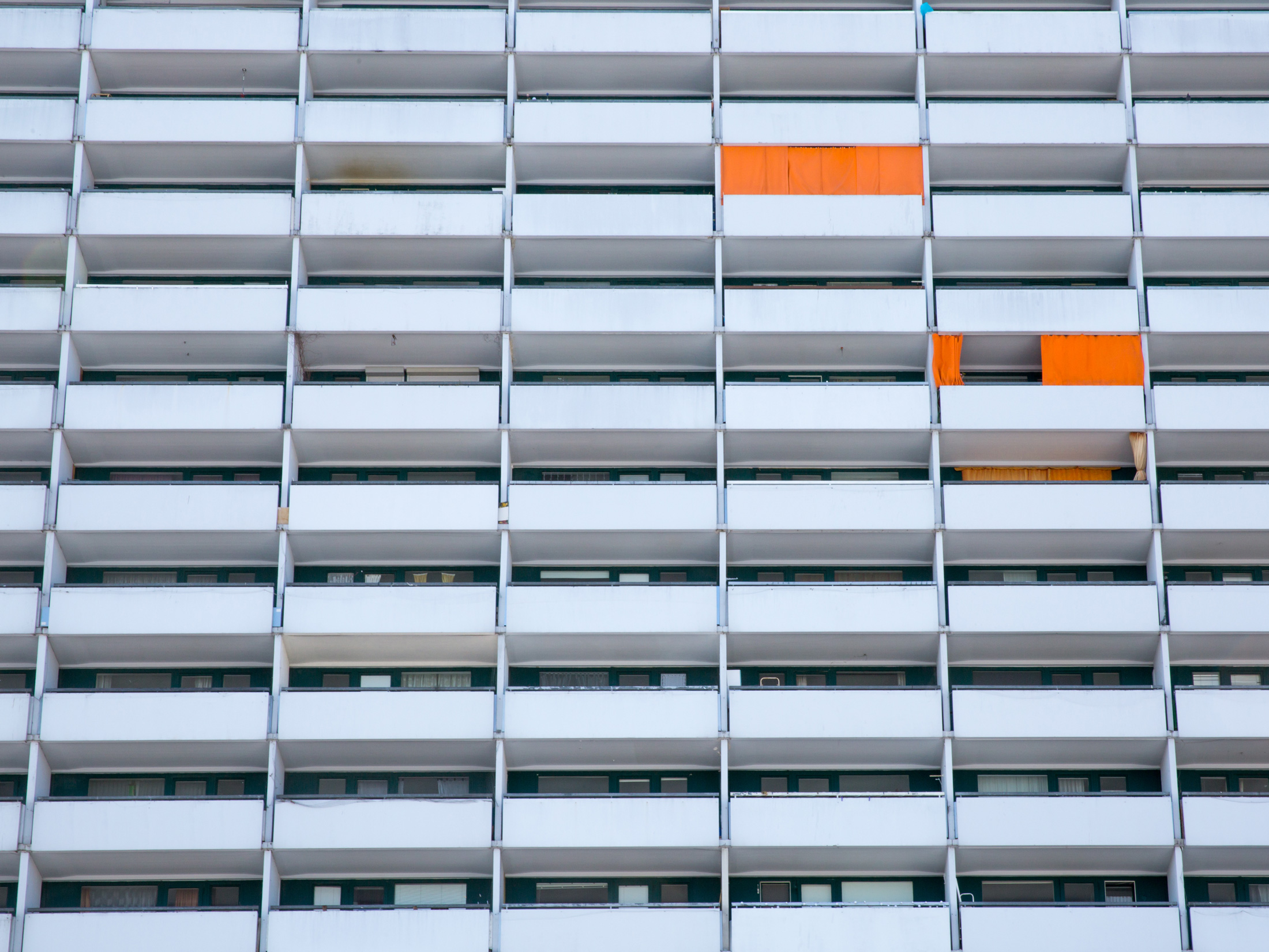 vereinzelt knall-orangene Vorhänge vor einer balkonierten Häuserfassade