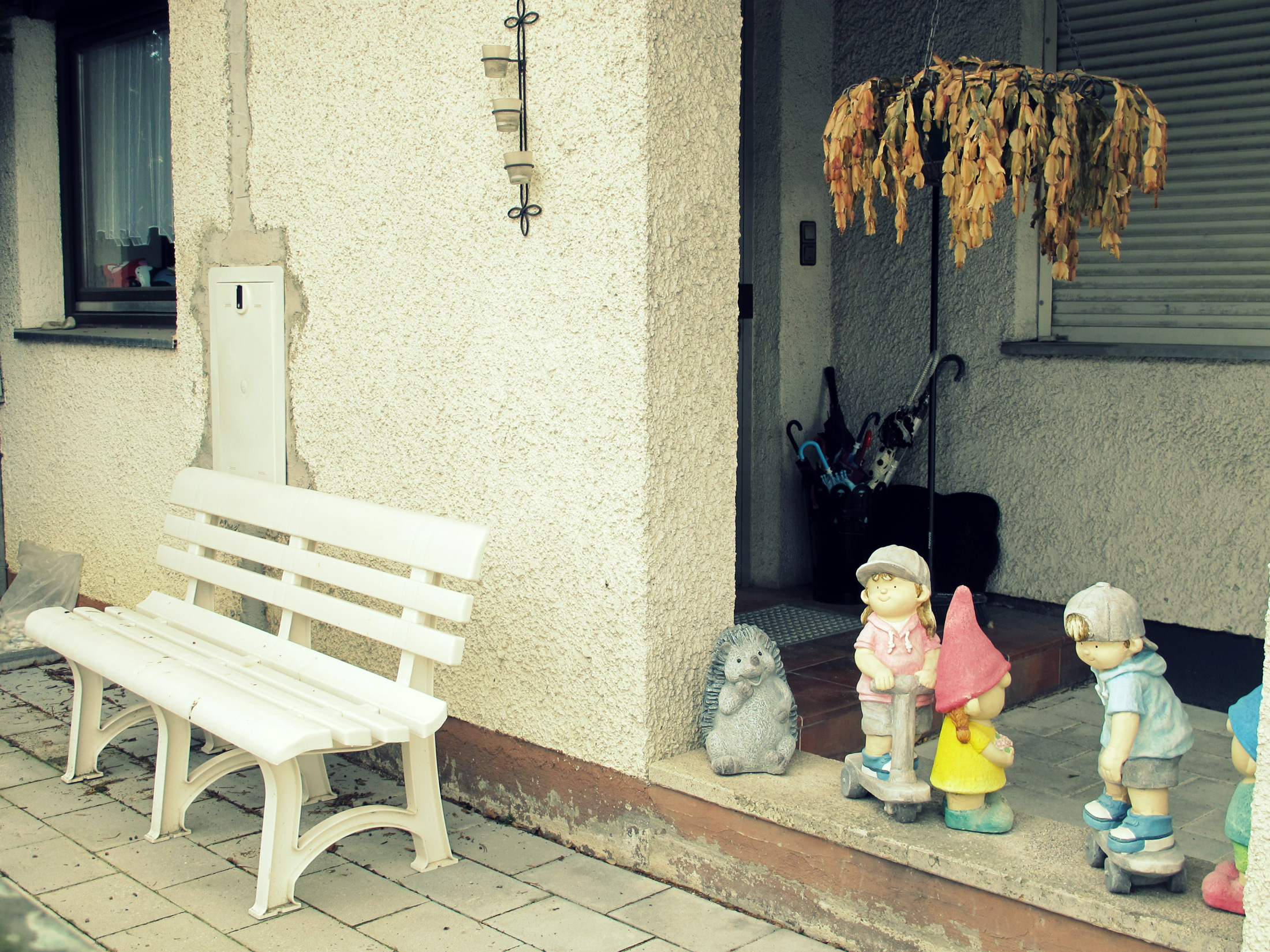 ausgeblichene Gartenzwerge und Kinderfiguren am Eingangsbereich eines Einfamilienhauses